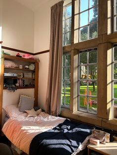 a bed sitting under two windows next to a book shelf filled with lots of books