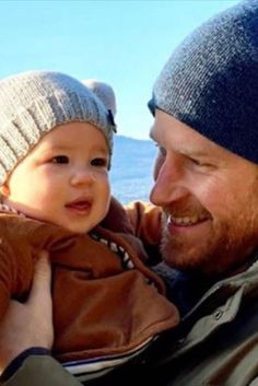 a man holding a baby in his arms and wearing a beanie on top of him