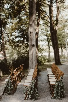 an outdoor ceremony setup with wooden chairs and greenery on the back, surrounded by trees