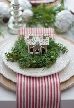 a christmas table setting with red and white striped napkins, silver ornaments and small gingerbread house