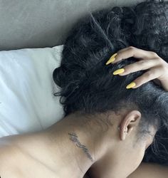 a woman with yellow nail polish laying on top of a bed next to her hair