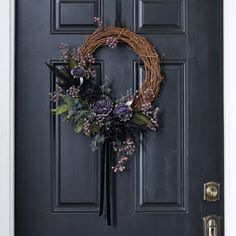 a wreath on the front door with purple flowers and greenery hanging from it's side