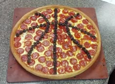 a pizza with pepperoni and olives on a cutting board in the shape of a peace sign