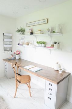 a wooden desk sitting under a window next to a shelf filled with books and plants