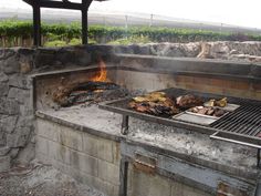 a bbq grill with food cooking on top of it next to a stone wall