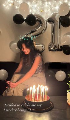 a woman sitting in front of a birthday cake with candles on it and balloons behind her