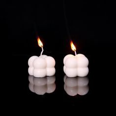 two candles that are shaped like clouds on a black surface, with one candle lit in the shape of a cloud