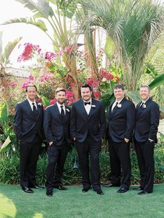 a group of men standing next to each other wearing black suits and bow ties with flowers in the background