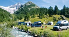 several campers are parked near a stream in the mountains