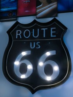 the route 66 sign is lit up in front of several pictures on the wall behind it