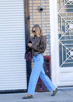 a woman is walking down the sidewalk while looking at her cell phone and carrying a purse