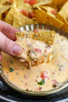 a hand holding a tortilla chip over a bowl of quesadilla dip