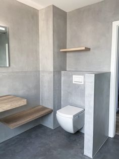 a white toilet sitting inside of a bathroom next to a wooden counter and shelf on the wall