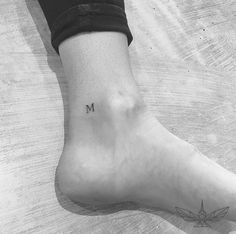 a person's foot with the letter m tattooed on their left leg and an arrow tattoo on the right ankle