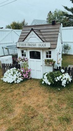 a small white shed with flowers growing out of it's roof and the words farm fresh iggs written on the door