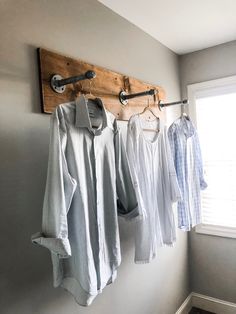 three shirts hanging on the wall in front of a window and a coat rack with clothes