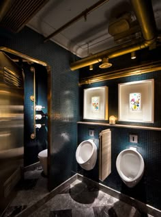 two white urinals in a bathroom with blue tile walls and gold trimming