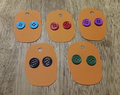 four different colored buttons are placed next to each other on a wooden table with orange tags