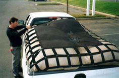 a man unloading a bed in the back of a white truck with black netting on it