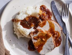 a white plate topped with meat covered in gravy and mashed potatoes next to a fork