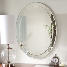 a round mirror sitting on top of a wooden table next to a lamp and clock