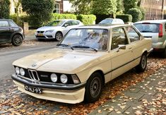 an old bmw is parked on the side of the road in front of other cars