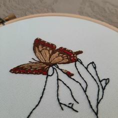 a close up of a hand holding a butterfly on a white cloth with red thread