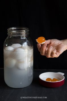 a person holding an orange in front of a mason jar filled with ice