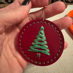 a hand holding a red ornament with a green christmas tree on the front