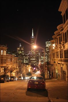 a red car parked on the side of a road in front of tall buildings at night