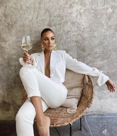 a woman sitting on a wicker chair holding a glass of wine in her hand