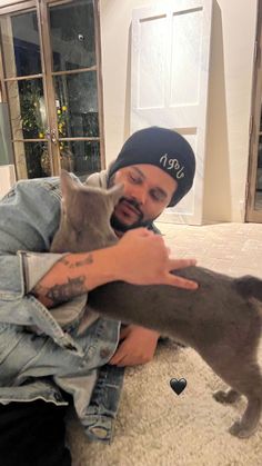 a man holding two cats in his arms while sitting on the floor next to him