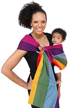 a woman holding a baby wrapped in a rainbow colored ring sling on her shoulder and smiling at the camera