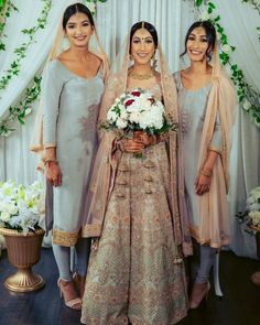 three women standing next to each other in front of a white backdrop with flowers and greenery