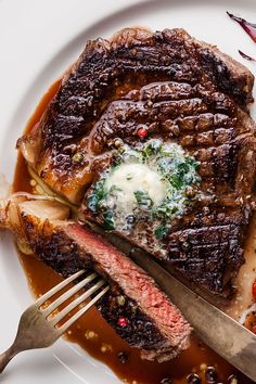 a steak with sauce and vegetables on a white plate next to a knife and fork