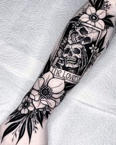 a black and white tattoo on the arm with flowers, skull and card reading the love story