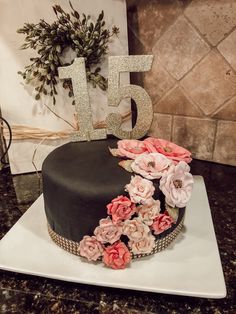 a black and pink cake with flowers on top sitting on a table next to a number 15 sign