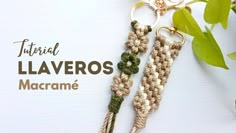 two crocheted tassels hanging from hooks on a white surface with green leaves