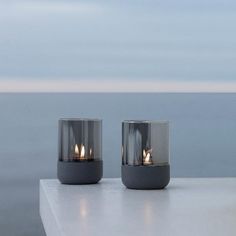 two lit candles sitting on top of a white table next to the ocean and sky