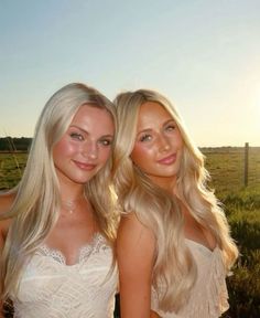 two beautiful young women standing next to each other in front of a green grass covered field