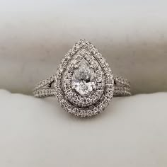 a white gold ring with a pear shaped diamond surrounded by smaller round brilliant cut diamonds