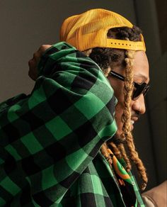 a man with dreadlocks wearing a yellow hat and green checkered hoodie