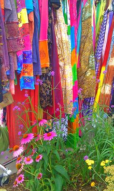 there are many different colored clothing hanging on the clothesline and flowers in front of them