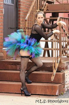 a woman is posing on the steps wearing a blue and green outfit with feathers in her skirt