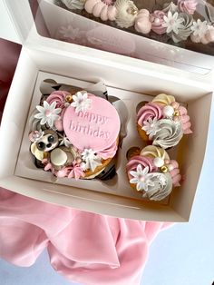 two cupcakes with pink frosting and white flowers are in a gift box