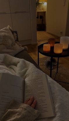 a person laying in bed reading a book with candles on the side table next to them