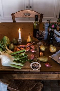 a wooden table topped with different types of vegetables and fruits next to a lit candle