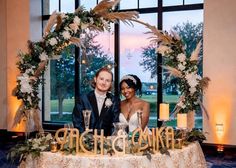 two people sitting at a table in front of a window with candles and flowers on it