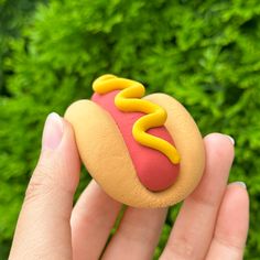 a hand holding a toy hot dog with mustard and ketchup on it's bun