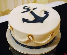 a white and blue cake with an anchor on top is sitting on a black table